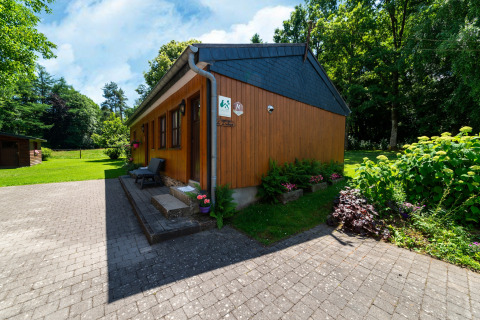 Afbeelding van het houten lodge ‘Les Bouleaux’ in België, omringd door een groene tuin en bomen.