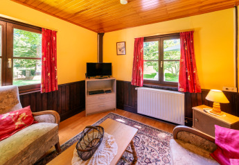 Cozy living room at 'Les Bouleaux' lodge in Belgium featuring red curtains, wood details, and armchairs.