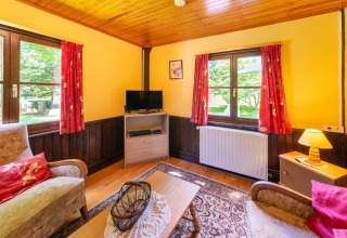 Gezellige woonkamer in lodge 'Les Bouleaux' in België met rode gordijnen, houten details en lichtinval.