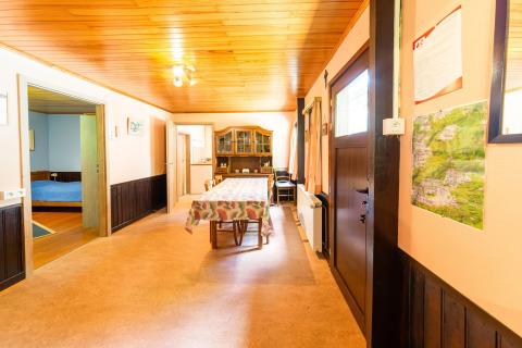 Eetkamer in lodge Les Bouleaux in België met houten plafond, tafel, kaart aan de muur en toegang tot slaapkamer.