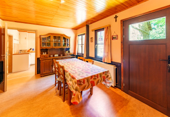 Dining room with wooden ceiling, furniture, and kitchen view in lodge «Les Bouleaux» in Belgium.