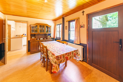 Eetkamer met houten plafond, meubels en keukenuitzicht in lodge «Les Bouleaux» in België.