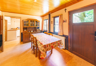Eetkamer met houten plafond, meubels en keukenuitzicht in lodge «Les Bouleaux» in België.