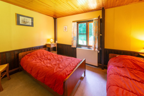 Kamer in lodge 'Les Bouleaux' in België met twee eenpersoonsbedden, gele muren en houten plafond.