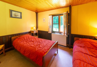 Kamer in lodge 'Les Bouleaux' in België met twee eenpersoonsbedden, gele muren en houten plafond.