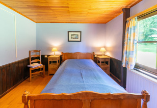 Sfeervolle slaapkamer in Les Bouleaux-lodge in België met eenpersoonsbed, houten meubelen en raam.