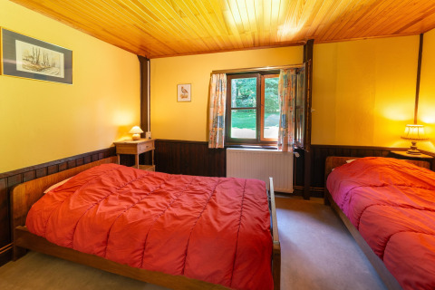Heldere kamer in lodge Les Bouleaux in België met twee eenpersoonsbedden en rode dekbedden.