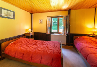 Heldere kamer in lodge Les Bouleaux in België met twee eenpersoonsbedden en rode dekbedden.