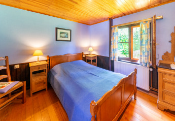 Cozy bedroom at Les Bouleaux lodge in Belgium, featuring wooden furniture, blue bedcover, and sunny window.