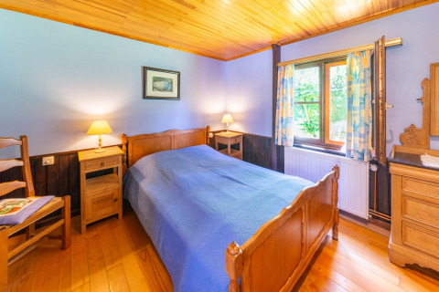 Knusse slaapkamer in lodge Les Bouleaux in België, met houten meubels en blauwe sprei, veel daglicht.
