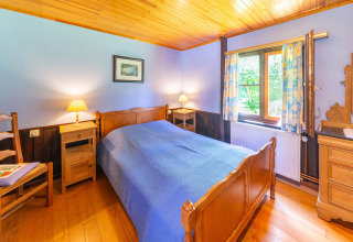 Knusse slaapkamer in lodge Les Bouleaux in België, met houten meubels en blauwe sprei, veel daglicht.