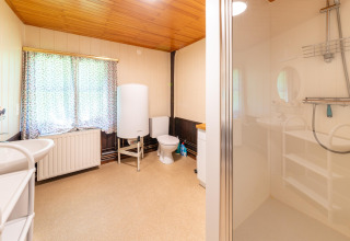 Lichte en ruime badkamer in lodge 'Les Bouleaux' in België met douche, toilet en groot raam.