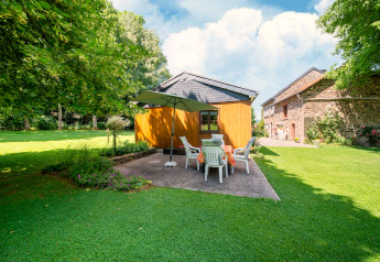 Garden area at lodge 'Les Bouleaux' in Belgium, patio set with umbrella and a wooden outbuilding.