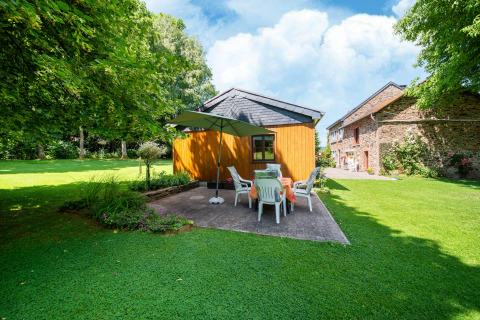 Tuin bij lodge 'Les Bouleaux' in België met terras, parasol, zitgroep en houten bijgebouw.