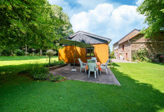 Tuin bij lodge 'Les Bouleaux' in België met terras, parasol, zitgroep en houten bijgebouw.