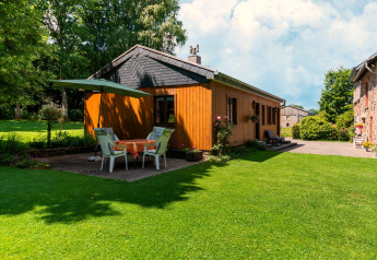 Cozy wooden lodge at Les Bouleaux in Belgium with outdoor dining area, umbrella, and lush green lawn.