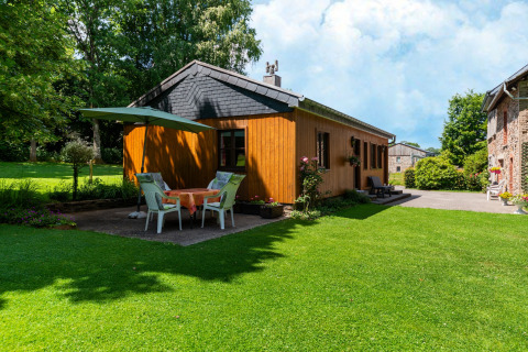 Knus houten huisje bij Les Bouleaux in België, met buitentafel, parasol en groene tuin.