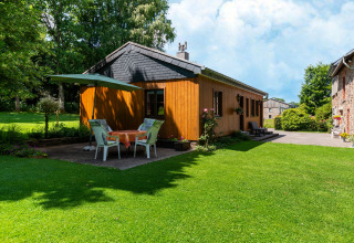 Knus houten huisje bij Les Bouleaux in België, met buitentafel, parasol en groene tuin.