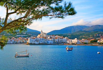 Vista costera de Castelló d'Empúries en Cataluña, España, con barcos, mar y montañas al fondo.
