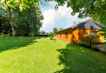 View of lodge «Les Bouleaux» in Belgium with green lawn, surrounding trees, and clear blue sky.