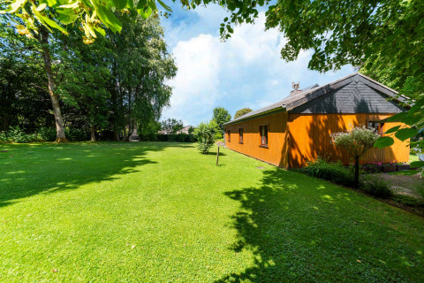 Uitzicht op lodge «Les Bouleaux» in België met grasveld, bomen en een heldere blauwe lucht.
