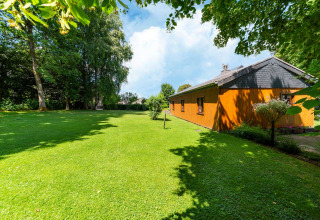 Uitzicht op lodge «Les Bouleaux» in België met grasveld, bomen en een heldere blauwe lucht.