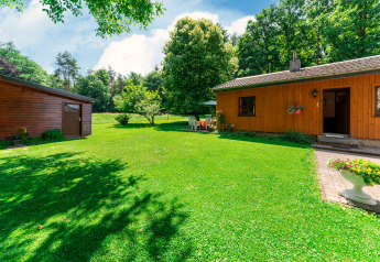 Outdoor view of the lodge «Les Bouleaux» in Belgium, featuring a green lawn, trees, and wooden buildings.