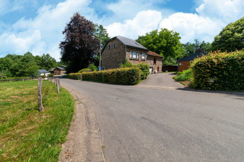 Straatbeeld met stenen lodge en groene heggen bij Les Bouleaux, gelegen in het landelijke België.