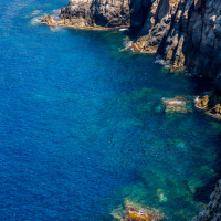 Rocky coastline and clear blue sea near Alghero in Sardinia, Italy, showing beautiful water shades.