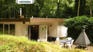 Rustico lodge The Deer Forest con patio, sedie da giardino e camino esterno immerso nel verde bosco.