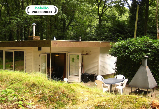 Lodge chaleureux The Deer Forest avec terrasse, mobilier de jardin et barbecue en pleine forêt verdoyante.