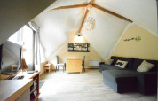 Stue i chalet 'Mise Au Vert' i Belgien med skrå loft, stor sofa, tv og spiseområde under træbjælker.
