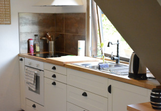 Moderne keuken met witte kasten, fornuis, gootsteen en raam in chalet Mise Au Vert in België.