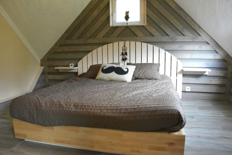 Slaapkamer met houten panelen, groot bed, bruine sprei en snor kussen in chalet Mise Au Vert, België.