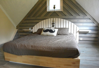 Slaapkamer met houten panelen, groot bed, bruine sprei en snor kussen in chalet Mise Au Vert, België.