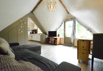 Lyst skråtagsstue i chalet 'Mise Au Vert' i Belgien med sofa, TV, spisebord og udsigt til haven.