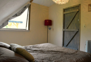 Schlafzimmer mit Schrägdach, offenem Fenster und Holztür im Chalet „Mise Au Vert“ in Belgien.