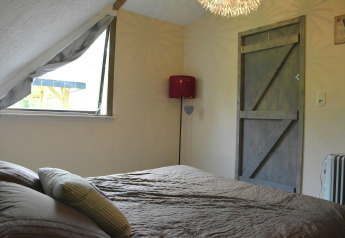 Soveværelse med skrå loft, åbent vindue, trædør og moderne belysning i chalet "Mise Au Vert", Belgien.
