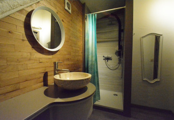 Moderne badeværelse i Mise Au Vert-chalet i Belgien med trævægge, rundt spejl og brusekabine.