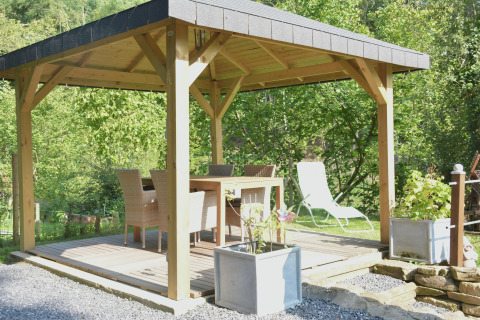 Overdekt terras met eettafel en stoelen bij chalet 'Mise Au Vert', omgeven door groen in België.