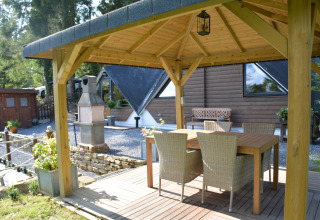 Overdekt terras bij chalet 'Mise Au Vert' in België met een houten tafel en vier rotanstoelen.