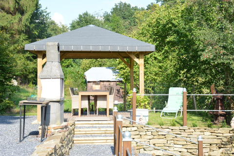 Buitenterras bij chalet 'Mise Au Vert' in België met prieel, barbecue en eetgedeelte in een groene tuin.