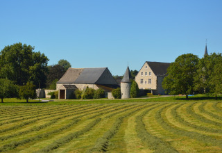 Foto van chalet 'Mise Au Vert' in België, met groene grasvelden, bomen en oude stenen gebouwen.