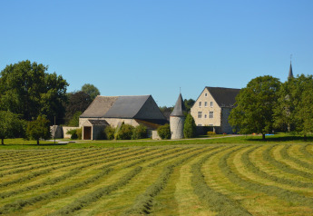 Foto af chalet 'Mise Au Vert' i Belgien, med grønne marker, træer og en historisk stenbygning.