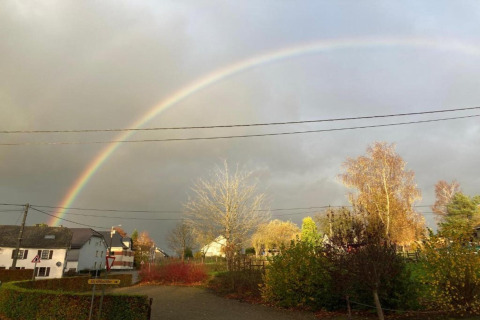 Regenboog boven een dorp, gezien vanaf chalet 'Mise Au Vert' in België op een bewolkte namiddag.