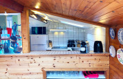 Pequeña cocina moderna en cabaña de madera con azulejos blancos, electrodomésticos y platos decorativos.
