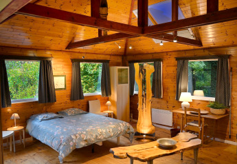 Dormitorio con paredes de madera en la cabaña Quarreux 27 en Bélgica, con grandes ventanas y luz cálida.