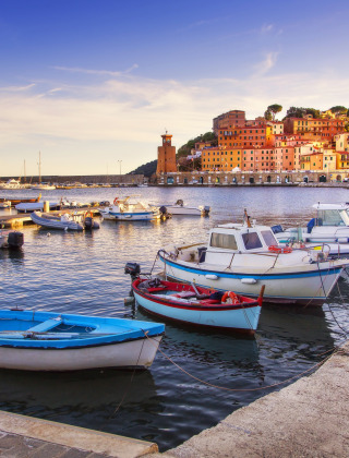 Boote im Hafen von Lacona, umgeben von bunten Häusern und grünen Hügeln in der Toskana, Italien.
