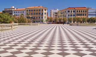 Plaza amplia con suelo de patrón ajedrezado en Lacona, Toscana, Italia, rodeada de pintorescos edificios.
