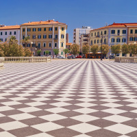Plaza amplia con suelo de patrón ajedrezado en Lacona, Toscana, Italia, rodeada de pintorescos edificios.